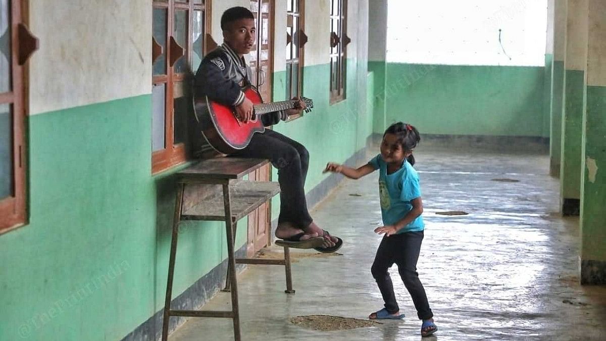 Joshua sits on a bench in one corner of the camp’s corridor, playing a love song on his guitar, while a little girl dances to the tune | Praveen Jain | ThePrint
