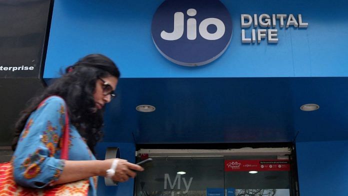 A woman checks her mobile phone as she walks past a mobile store of Reliance Jio | Reuters/Shailesh Andrade/File Photo