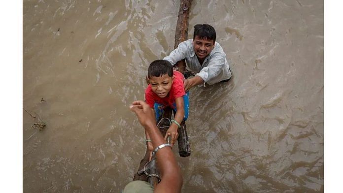 A man helps his son to climb onto a flyover under construction, after being displaced by the rising water level of river Yamuna in New Delhi | Reuters/Adnan Abidi