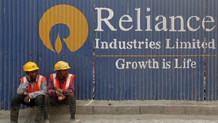 Labourers rest in front of an advertisement for Reliance Industries at a construction site in Mumbai, India | Reuters