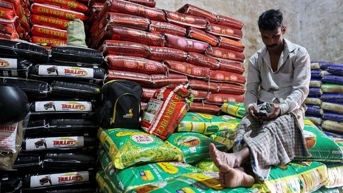 A man sits on rice packets inside a store room, at a wholesale market in Navi Mumbai, India | Reuters