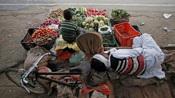 A vendor sleeps as his son waits for customers at their roadside vegetable shop in New Delhi | Reuters
