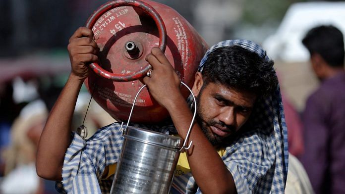 A man carries an LPG cylinder on his shoulder at a wholesale market in the old quarters of Delhi, India | Reuters