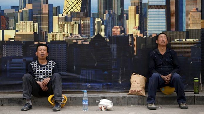 Construction workers take a nap in front of a wall of a construction site during their lunch break in Beijing | Reuters file photo