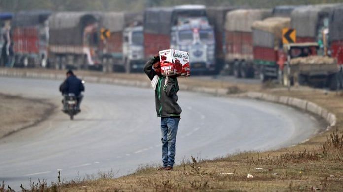 A man carries a box of apples next to parked supply trucks loaded with apples on a highway near Qazigund in south Kashmir's Anantnag district | Reuters