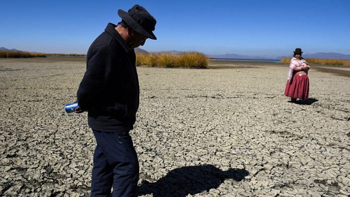 Gabriel Flores and Isabel Apaza walk on the dry, cracked bed near the shore of Lake Titicaca in drought season in Huarina, Bolivia | Reuters