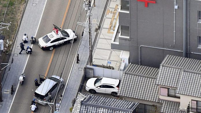 Police officers take cover behind cars outside the post office where a suspected gunman has taken people hostage after injuring two at a hospital, in Warabi, Saitama Prefecture, Japan October 31, 2023 | Mandatory credit Kyodo/via Reuters