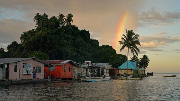 Local resident Tarusila Boseiwaqa walks along a sea wall that no longer protects homes from the intrusion of water at higher tides, as a rainbow forms over Serua Village, Fiji | Reuters