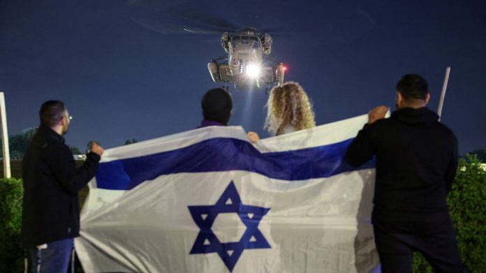 People hold an Israeli flag as a helicopter carrying hostages released amid a hostages-prisoners swap deal between Hamas and Israel arrives at Sheba Medical Center in Ramat Gan, Tel Aviv district, Israel | Reuters