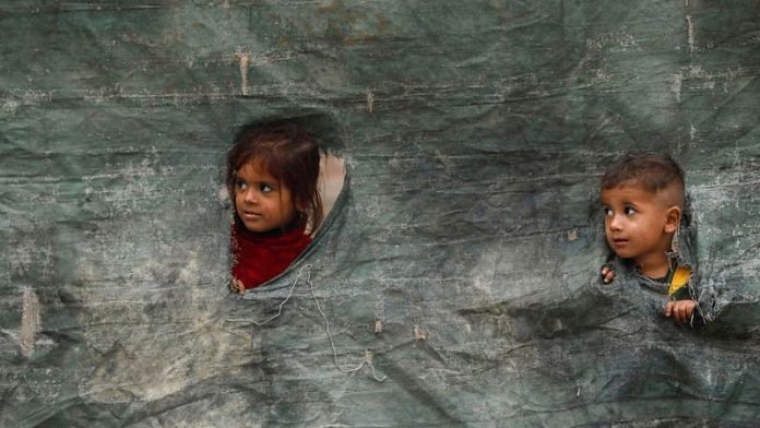 Children from an Afghan family look outside from a torn tent as they along with their family are returning home outside the UNHCR repatriation centres in Azakhel town in Nowshera, Pakistan, on 1 Nov 2023 | Reuters