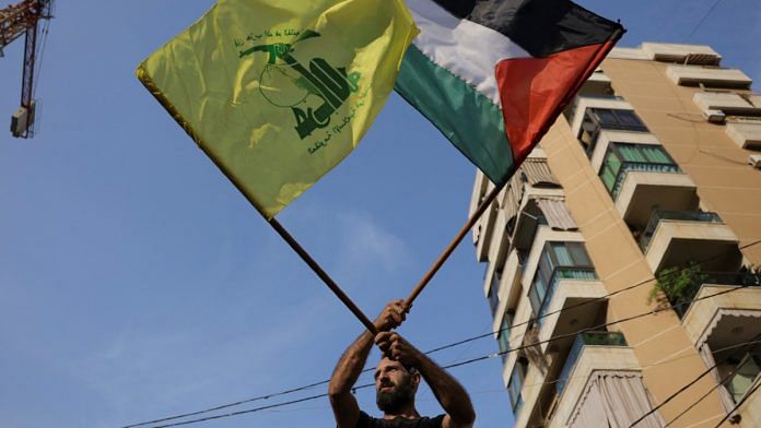 A man holds Hezbollah & Palestinian flags in Beirut on 27 Oct 2023 | Reuters/Amr Alfiky