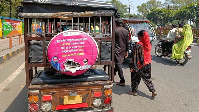 People walk past an e-rickshaw carrying a worn ad for MP government's Ladli Behna Yojana | Krishan Murari | ThePrint