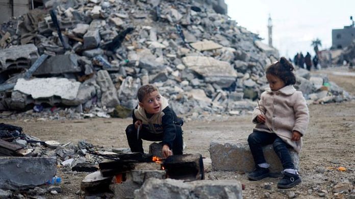 Palestinian children sit by the fire next to the rubble of a house hit in an Israeli strike in Khan Younis in the southern Gaza Strip | Reuters