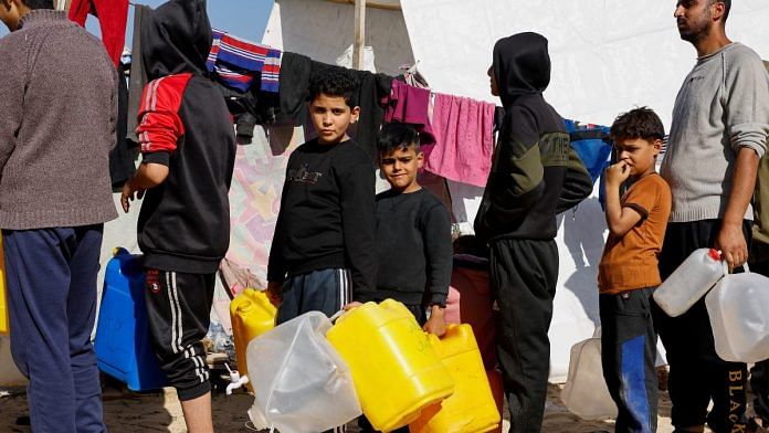 Boys hold containers while they line up, as displaced Palestinians, who fled their houses due to Israeli strikes, shelter in a tent camp near the border with Egypt | Reuters