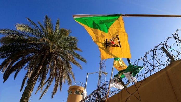 A member of Hashd al-Shaabi (paramilitary forces) holds a flag of Kataib Hezbollah militia group during a protest outside the main gate of the U.S. Embassy in Baghdad | Reuters file photo