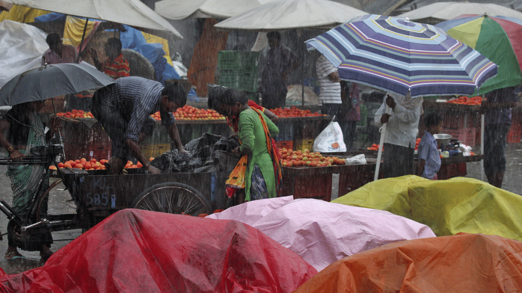 Vendors take shelter under plastic tarpaulins as others work during a heavy rain shower at a wholesale vegetable market in Chandigarh, India | File Photo | Reuters/Ajay Verma