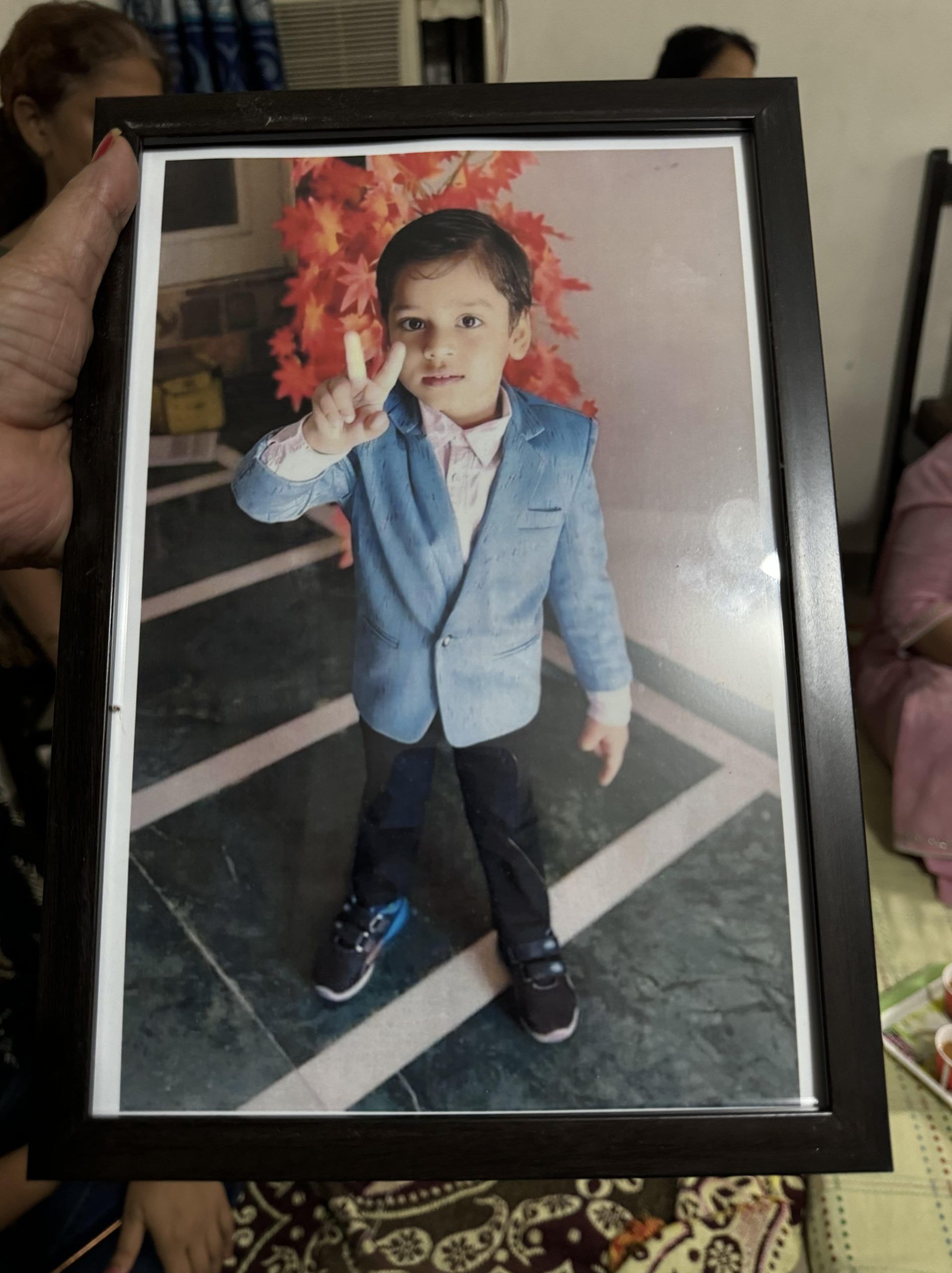 A family member holds a photograph of five-year-old Mevansh who drowned in the society’s swimming pool
