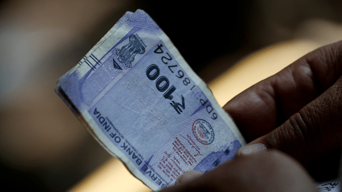 A customer holds hundred rupees Indian currency notes near a roadside currency exchange stall in New Delhi, India, May 24, 2024 | Reuters/Priyanshu Singh/File Photo