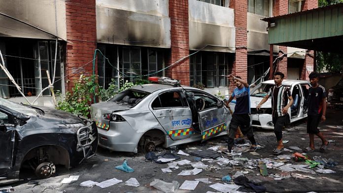 People walk next to vandalised cars at the Mohammadpur Police Station, after the resignation of Bangladeshi Prime Minister Sheikh Hasina, in Dhaka, Bangladesh, August 6, 2024 | Reuters