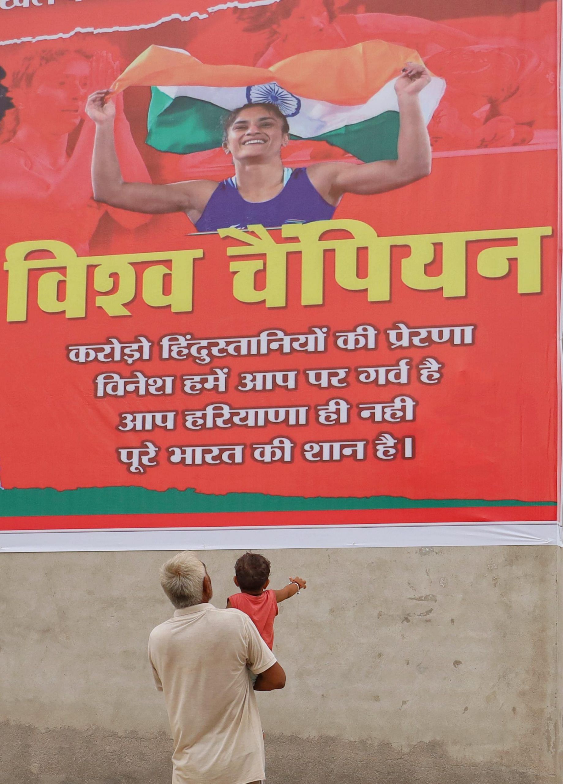 A toddler with her grandfather looks at the poster of Phogat | Photo: Manisha Mondal | ThePrint