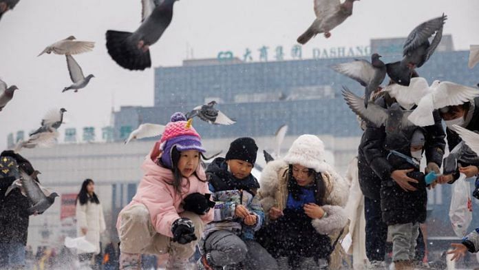 Children feed pigeons in Harbin, Heilongjiang Province, China, February 10, 2023. REUTERS/Thomas Peter/File Photo