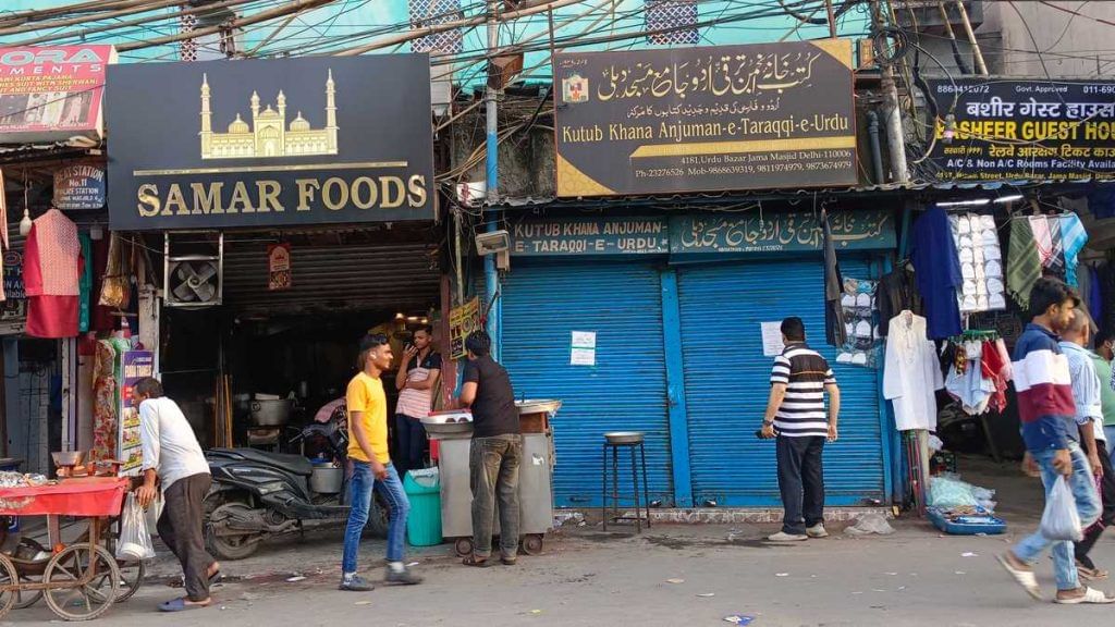 उर्दू बाज़ार की सबसे पुरानी किताबों की दुकानों में से एक कुतुब खाना अंजुमन-ए-तरक्की-ए-उर्दू, अक्सर बंद शटर के साथ जीवंत रहती है, जबकि एक कबाब बनाने वाला बाहर काम करता है. फोटो: अलमिना खातून | दिप्रिंट