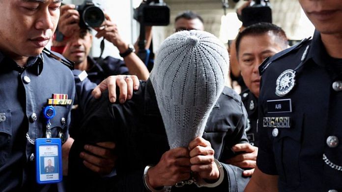 A man linked to Global Ikhwan Service and Business Holdings (GISB) covers his face as he is escorted by police officers after being charged in a court in Putrajaya, Malaysia September 18, 2024. REUTERS/Hasnoor Hussain