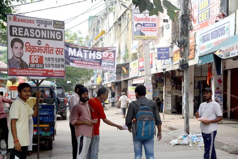 Mukherjee Nagarमुखर्जी नगर की तंग गलियों में कोचिंग क्लास के लिए पर्चे बांटे जा रहे हैं. कई छात्र पास में ही जूते के डिब्बे के आकार के कमरों में रहते हैं, और यूपीएससी के अपने सपनों को पूरा करने के लिए हर इंच स्थान का पूरा इस्तेमाल करते हैं. फोटो: सूरज सिंह बिष्ट | दिप्रिंट