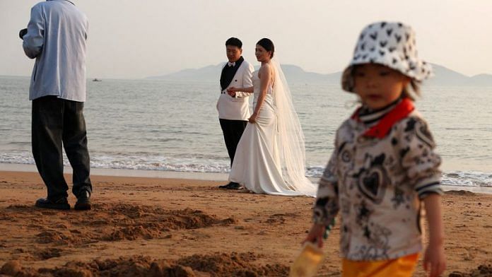 A child plays with sand near a couple taking part in a pre-wedding photoshoot on a beach in Qingdao, Shandong province, China April 21, 2024. REUTERS/Florence Lo/File Photo