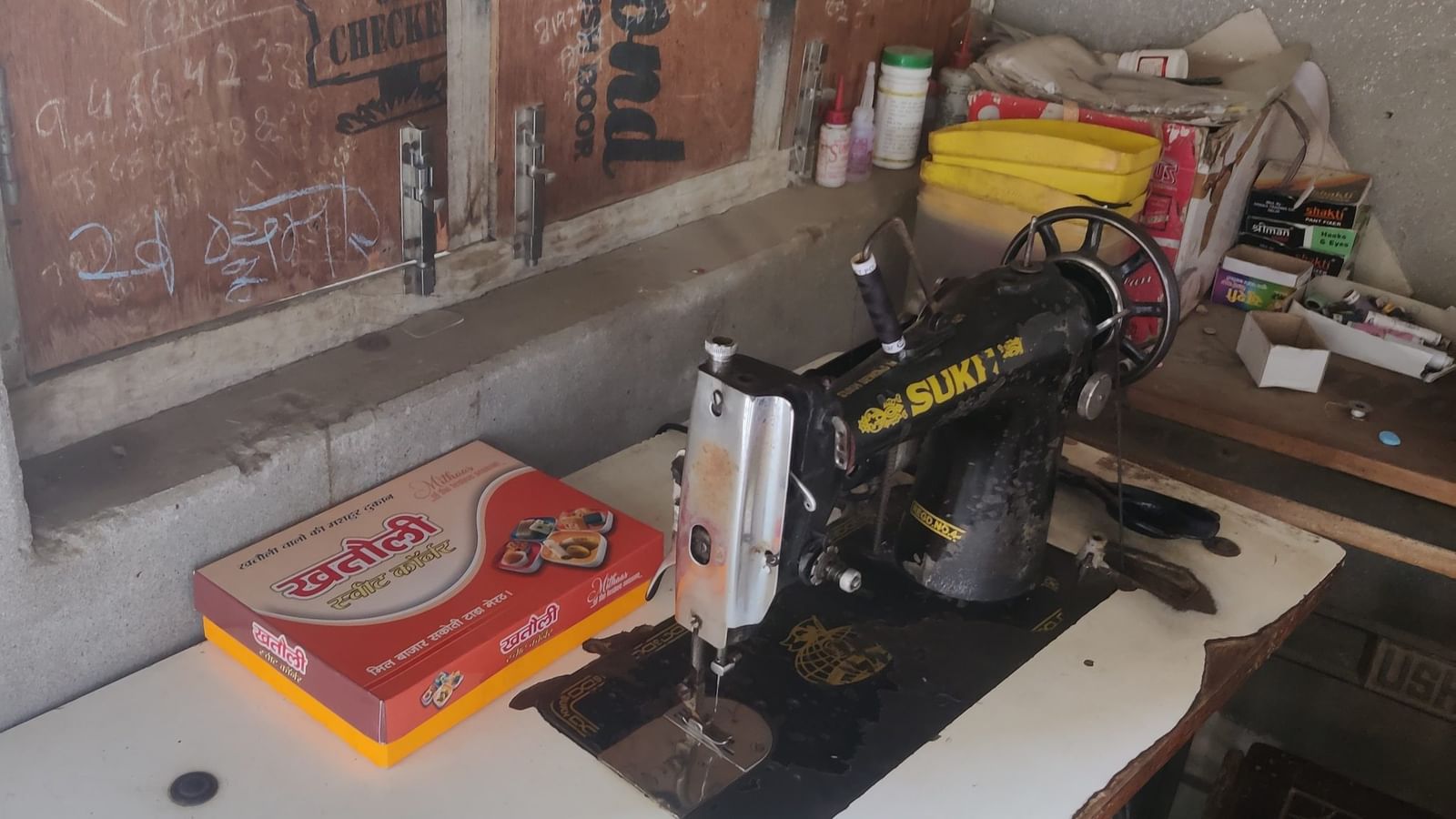 राजेंद्र कुमार की सिलाई मशीन के पास मिठाई का डिब्बा घर में आने वाले हर व्यक्ति, जिसमें पत्रकार भी शामिल हैं, उनके साथ बांटा जा रहा है | फोटो: अलमिना खातून/दिप्रिंट