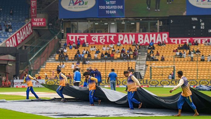 Ground staff cover the pitch during rains on the first day of the first test cricket match between India and New Zealand, at M Chinnaswamy Stadium in Bengaluru, Wednesday | PTI Photo/Shailendra Bhojak