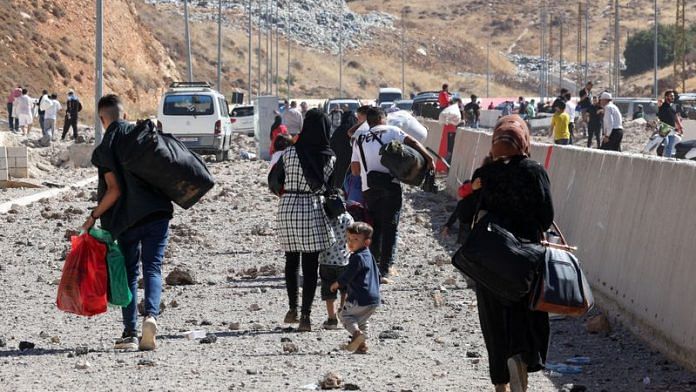 People carry their belongings while walking on the rubble, after an Israeli strike, as they flee Lebanon due to ongoing hostilities between Hezbollah and Israeli forces, at Masnaa border crossing with Syria, in Lebanon, October 4, 2024. REUTERS/Mohamed Azakir