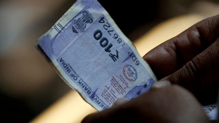 A customer holds hundred rupees Indian currency notes near a roadside currency exchange stall in New Delhi, India, 24 May 2024 | Priyanshu Singh | Reuters