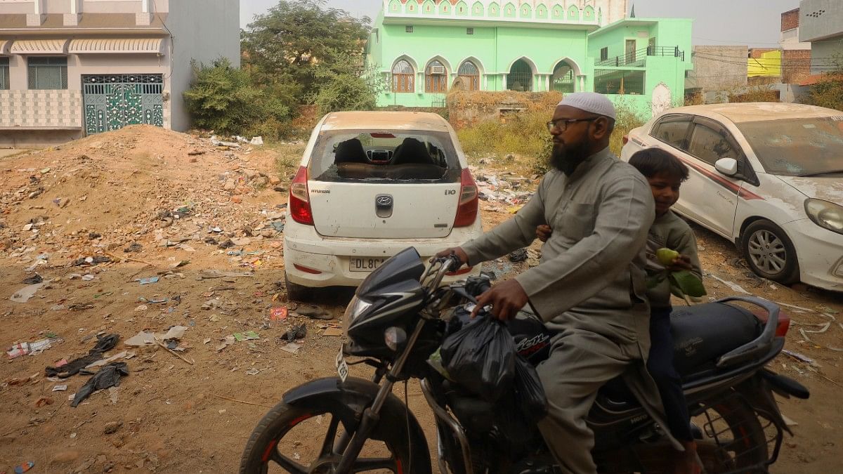 A man rides a motorcycle past vehicle vandalised during violence Sunday | Manisha Mondal | ThePrint