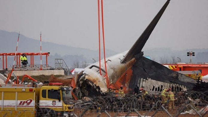 People stand as the wreckage of an aircraft lying on the ground after it went off the runway and crashed at Muan International Airport is pictured, in Muan, South Korea, 30 December 2024 | Reuters/Kim Soo-hyeon