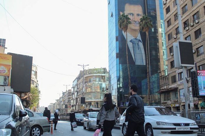 People walk near a poster depicting Syria's President Bashar al-Assad in Damascus, after last week's rebel seizure of Aleppo | Reuters