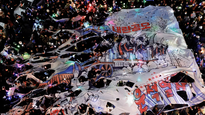 Protesters tear a banner depicting South Korean President Yoon Suk Yeol's face on a cartoon train, as they take part in a rally calling for the impeachment of South Korean President, who declared martial law, which was reversed hours later, near the headquarters of the ruling People Power Party in Seoul, South Korea, on 13 December 2024. | Kim Soo-hyeon | Reuters