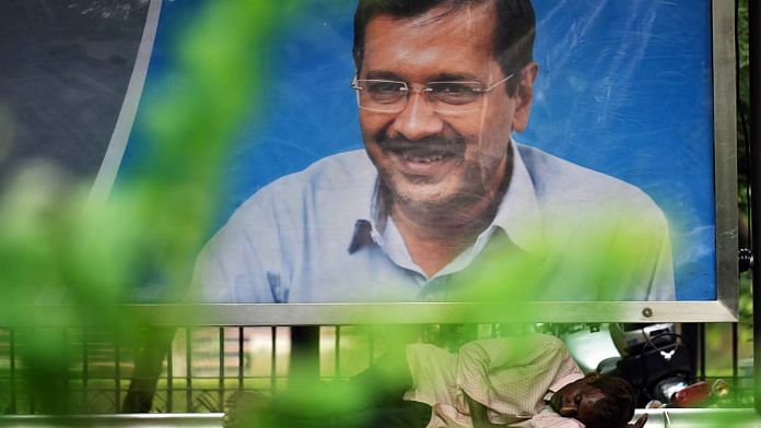 A man sleeps at a bus stop under a hoarding of Arvind Kejriwal in New Delhi | Photo: ANI