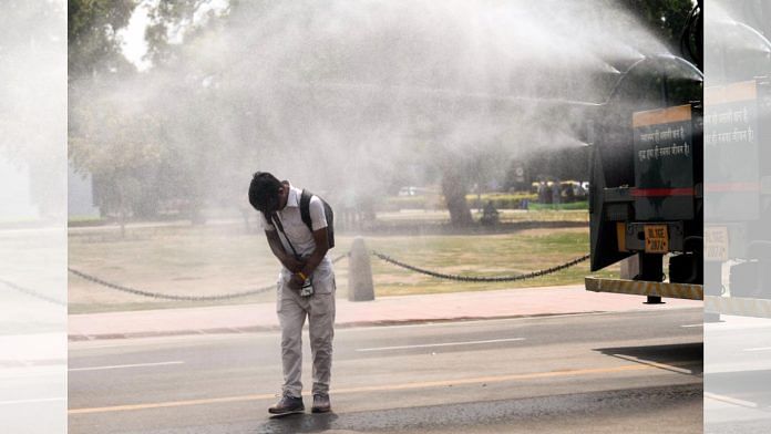 A boy cools himself from the tiny droplets of water from a truck-mounted sprinkler on a hot summer afternoon, at Kartavya Path in New Delhi. | ANI
