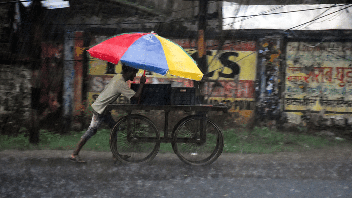 Representational image | A worker holding an umbrella pushes a cart amid heavy rainfall | ANI