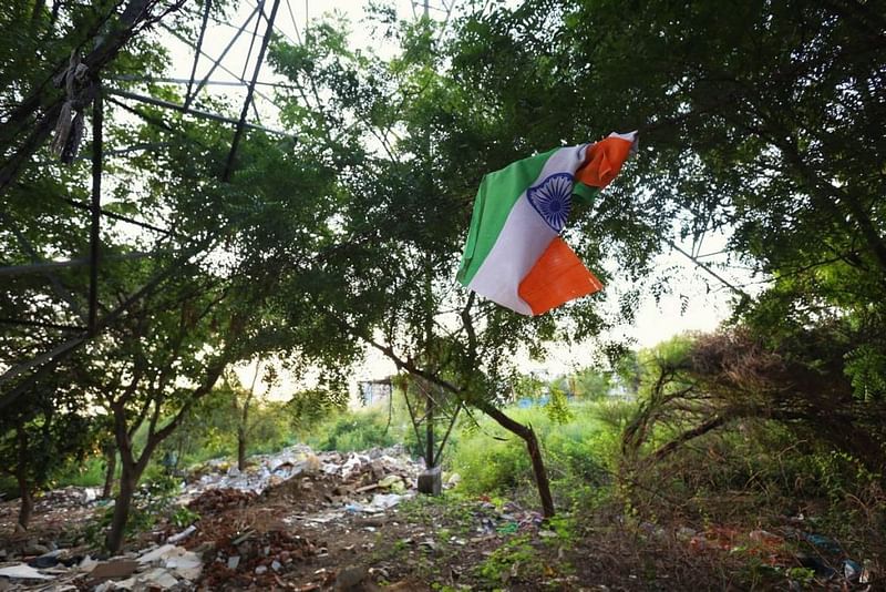 राजेश पायलट मार्ग पर एक तार से लटका फटा हुआ तिरंगा. पीछे सड़क किनारे जंगल में जमा कचरे का ढेर। | फोटो: मनीषा मोंडल/दिप्रिंट
