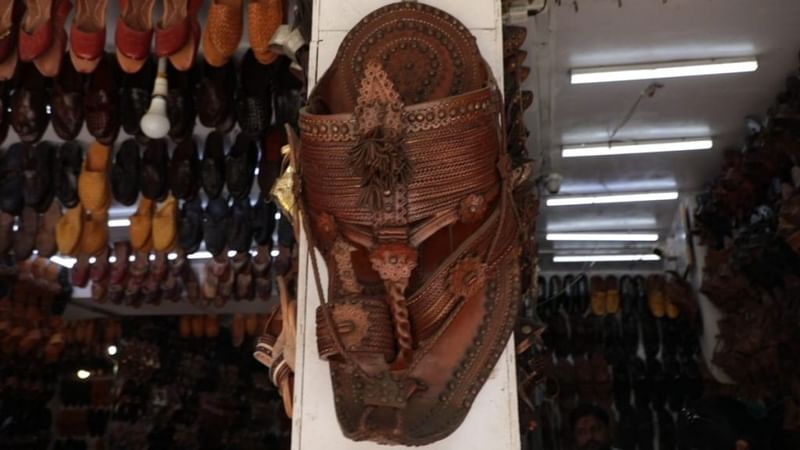 एक चप्पल की दुकान के बाहर कोल्हापुरी चप्पल की एक विशाल नकल टंगी है, जिसमें पारंपरिक बेल-बूटे, लटकन और बारीक कढ़ाई दिखती है | फोटो: मोहम्मद हम्माद/दिप्रिंट