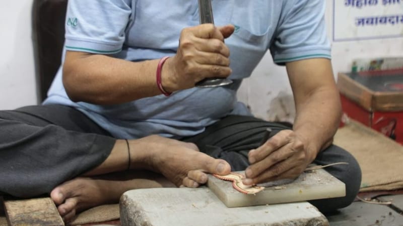 एक कारीगर चमड़े की पट्टी पर पारंपरिक डिज़ाइन की छाप लगाता है — जो कोल्हापुरी चप्पल का अहम हिस्सा बनती है | फोटो: मोहम्मद हम्माद/दिप्रिंट