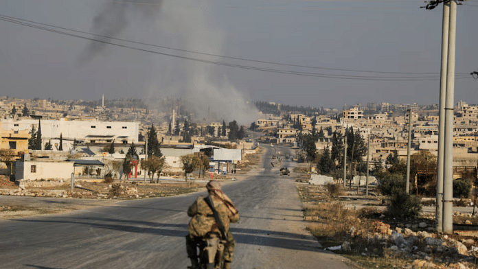Smoke rises as a member of the rebels led by the Islamist militant group Hayat Tahrir al-Sham drives on a motorbike in al-Rashideen, Aleppo province, Syria November 29, 2024 | Reuters