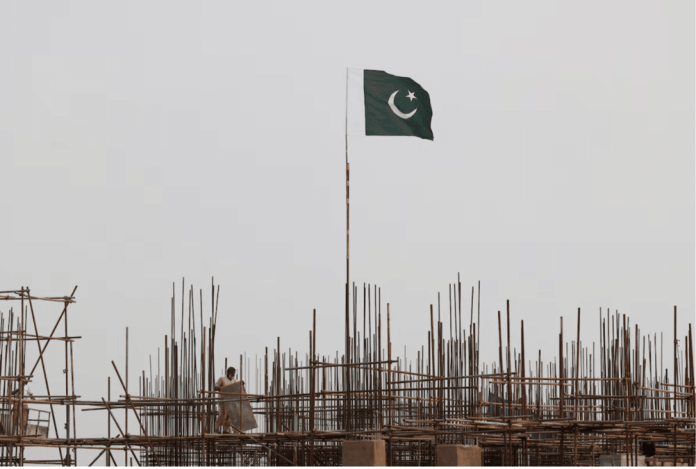 A Pakistani flag flutters over iron scaffoldings as a labourer works at a construction site on the eve of Pakistan's Independence Day celebrations, in Lahore, Pakistan August 13, 2025. REUTERS/Akhtar Soomro/File Photo