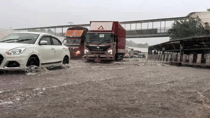 Commuters wade through waterlogged road due to heavy rain, in Gurugram on Monday | ANI