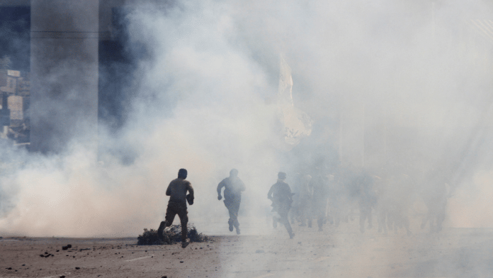 Police officers & supporters of Tehreek-e-Labbaik Pakistan (TLP) run amid tear gas fired by police during a solidarity march for Gaza in Lahore Sunday. | Reuters/Mohsin Raza