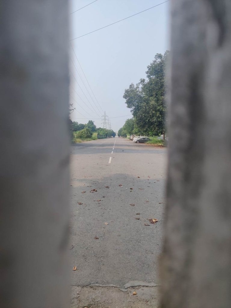 सहारा शहर के पिछले गेट की एक दरार से खाली सड़क और कंपनी की छोड़ी हुई गाड़ियां दिख रही हैं | फोटो: अमृतांश अरोड़ा/दिप्रिंट