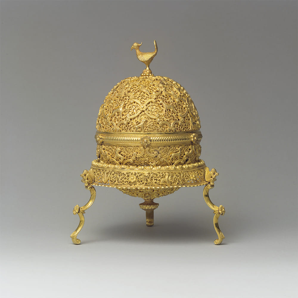 The gold case of a Goa stone. It is spherical and features intricate design, with a peacock at the top.