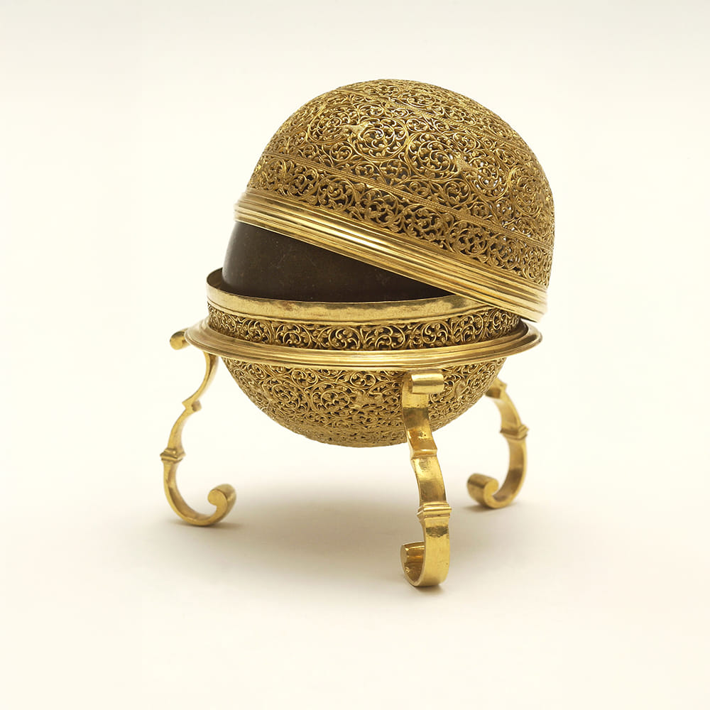 A Goa stone inside a case, with the lid partially lifted. This gold case is simpler and has a floral pattern.
